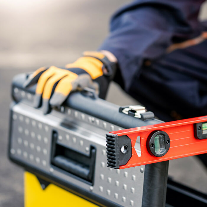 Male mechanic or maintenance worker man holding red aluminium spirit level tool or bubble levels and working tool box at construction site. Equipment for civil engineering project