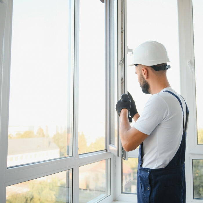 Construction worker repairing plastic window with screwdriver indoors, space for text. Banner design